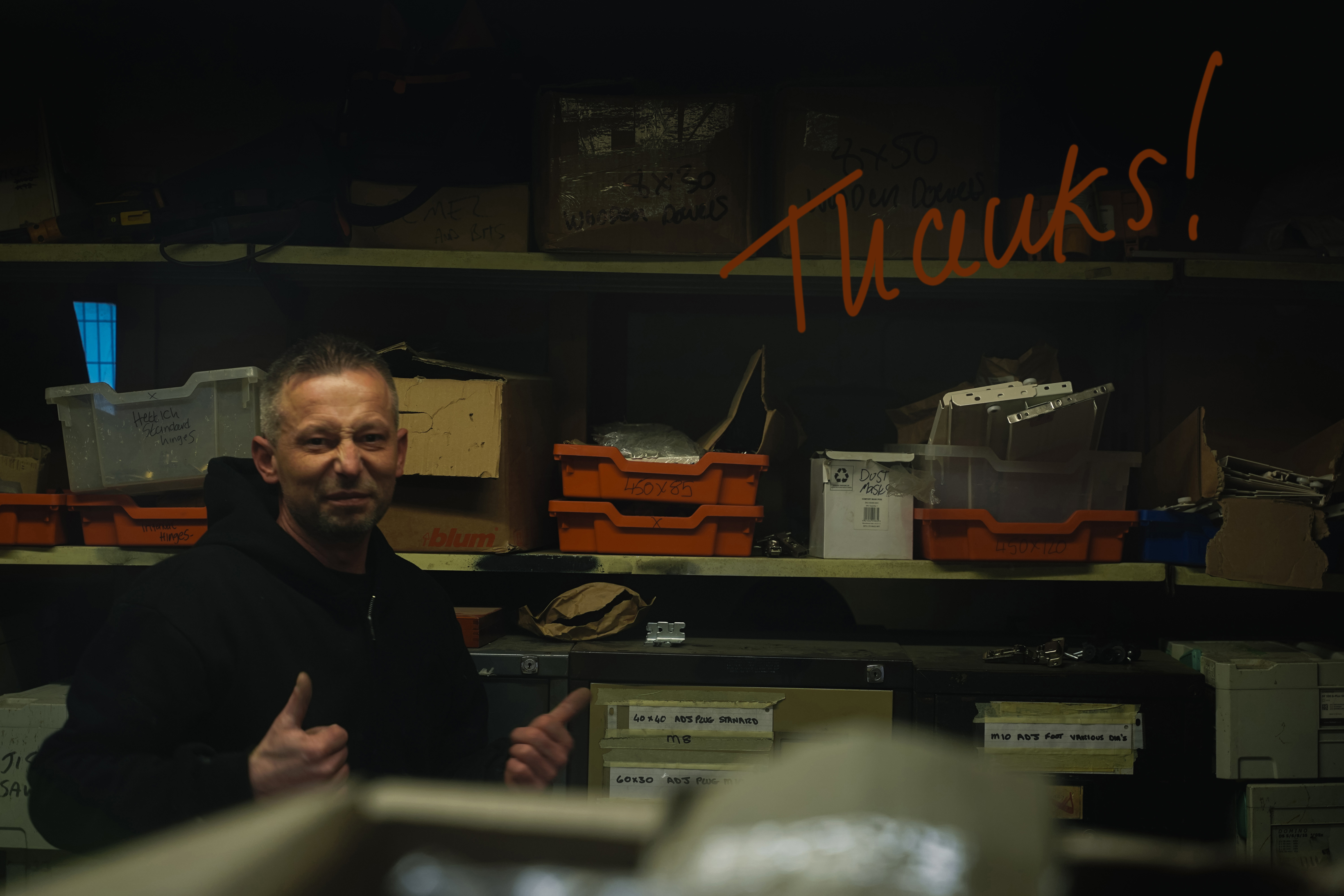 A photo of a Calfurn team member in a storage room, with their thumbs up, and the word 'Thanks!' written on the camera lens in orange marker pen.
